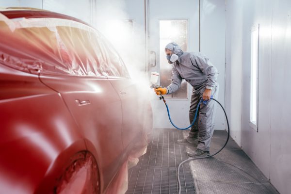 Automotive paint services, quality auto body shop concept. Painting the car in red color in the paint chamber on the service. S